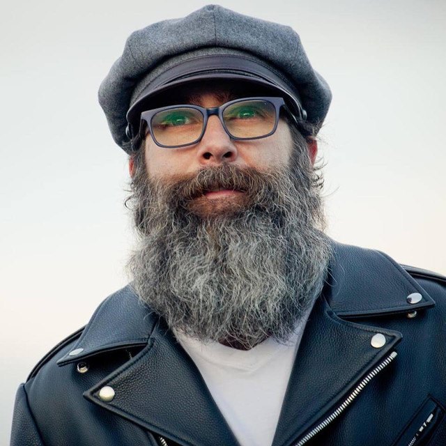 Estes Shane Whalen, in a flat cap and leather jacket, against an open sky.